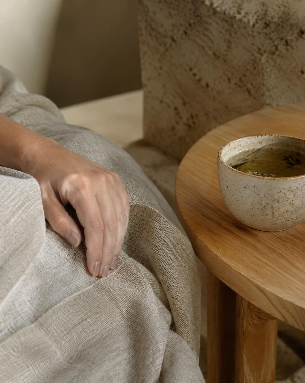 A hand resting on a linen blanket beside a cup of herbal tea